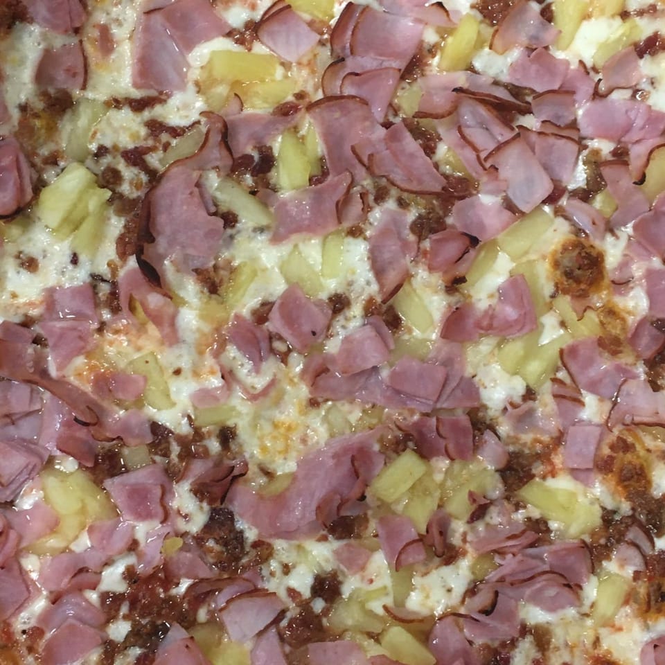 Close-up of a Hawaiian pizza from Amici Vicinato, topped with ham, pineapple, and melted cheese.