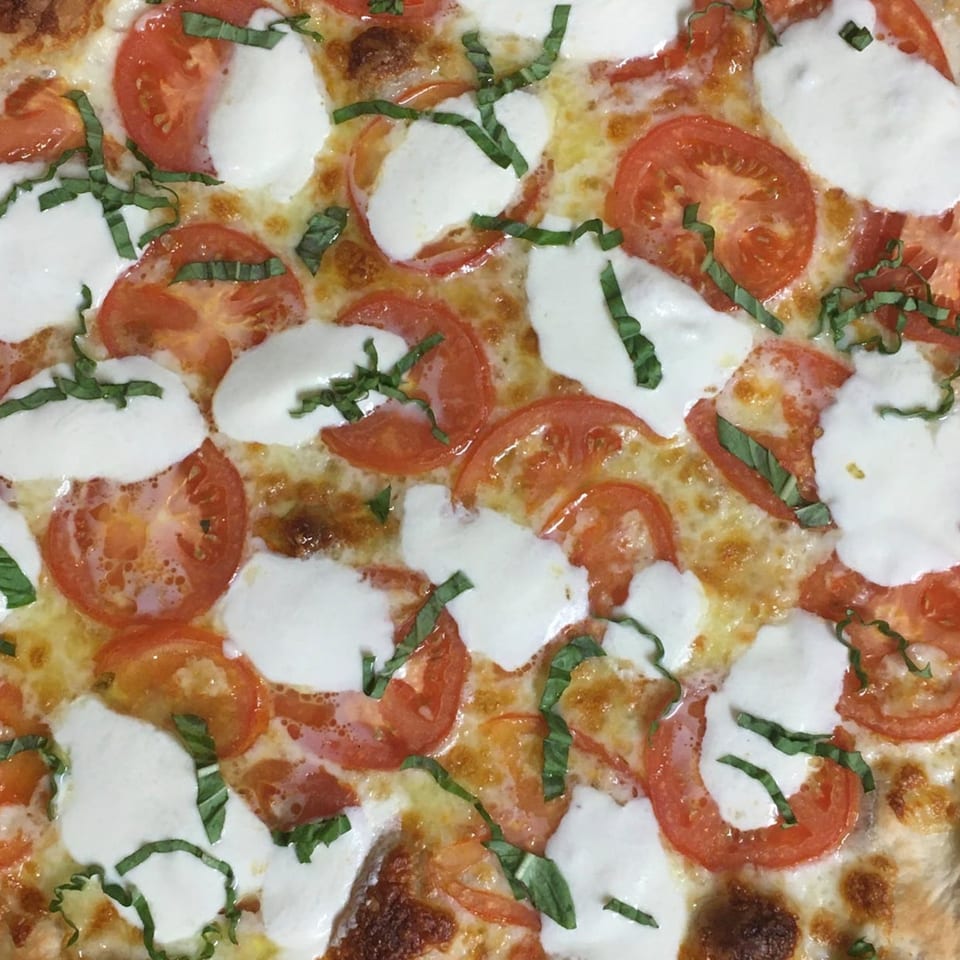 Close-up of a Margherita pizza from Amici Vicinato, topped with fresh mozzarella, sliced tomatoes, and basil.